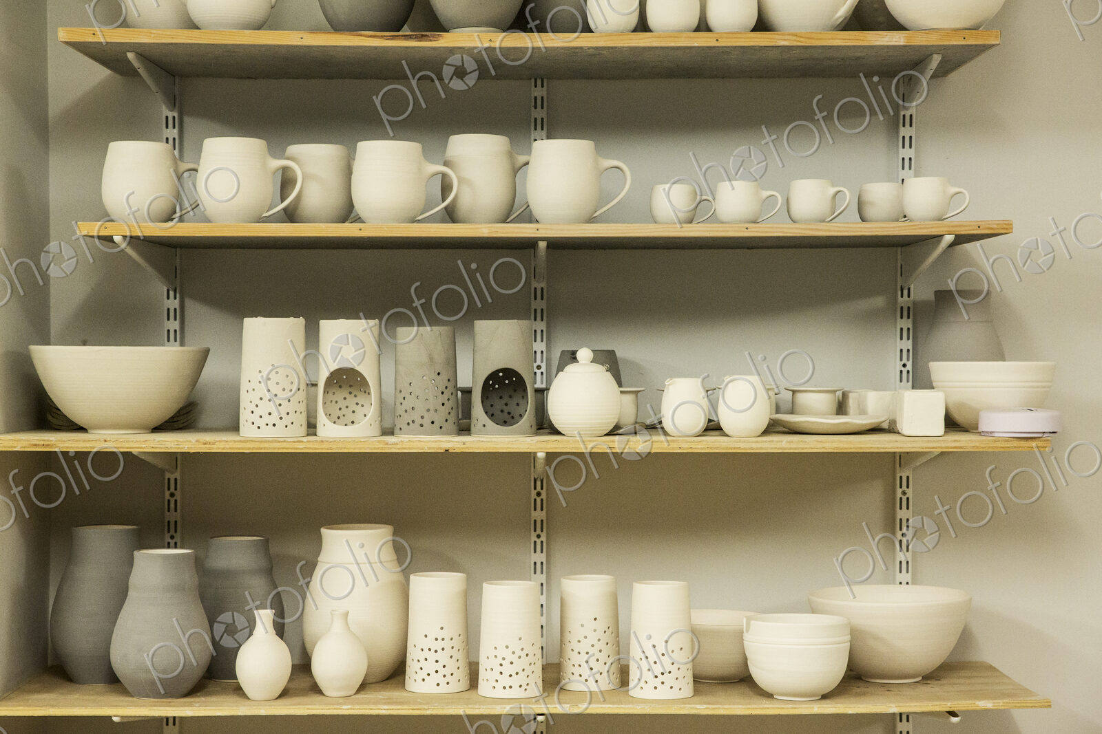 Racks of hand thrown hand crafted pottery vases and objects on shelves in the drying room.