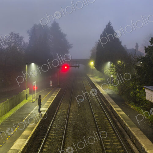 Railway station at dusk, single person on platform, red signal in the distance. Railway station at dusk, single person on platform, red signal in the distance.