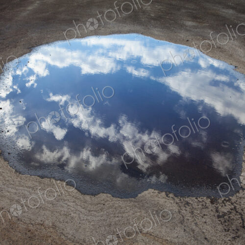 Rain drops falling onto a large puddle. A reflection of sky and clouds. Rain drops falling onto a large puddle. A reflection of sky and clouds.