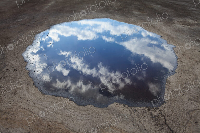Rain drops falling onto a large puddle. A reflection of sky and clouds.