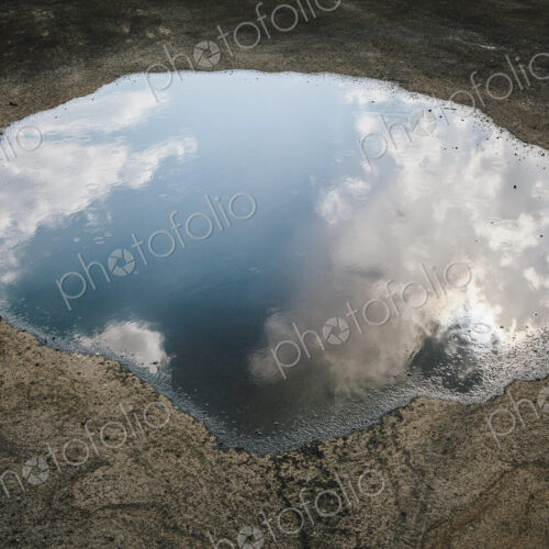 Rain drops falling onto a large puddle. A reflection of sky and clouds. Rain drops falling onto a large puddle. A reflection of sky and clouds.