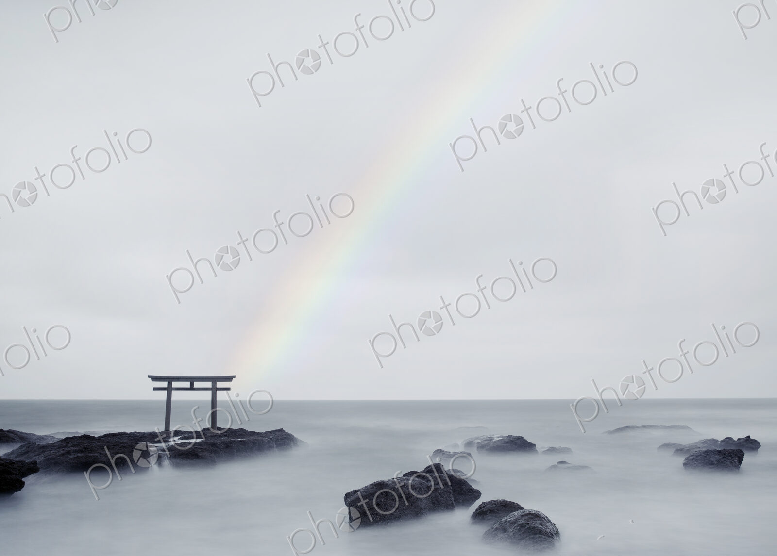 Rainbow over tall Torii gate on rocks in the middle of a lake.