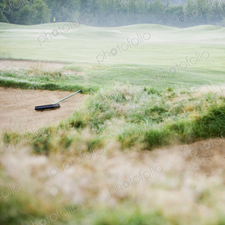 Rake in sand bunker on misty golf course.