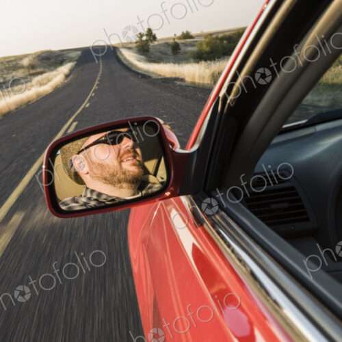 Rear view drivers mirror of a caucasian male driving a car on a road trip Rear view drivers mirror of a caucasian male driving a car on a road trip