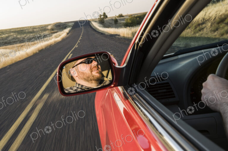 Rear view drivers mirror of a caucasian male driving a car on a road trip