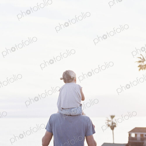 Rear view of a man carrying his young daughter on his shoulders. Rear view of a man carrying his young daughter on his shoulders.