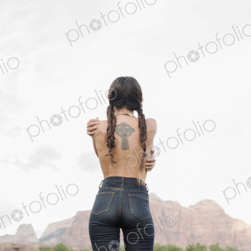 Rear view of a topless young woman with long brown hair in braids, wearing jeans,… Rear view of a topless young woman with long brown hair in braids, wearing jeans,…