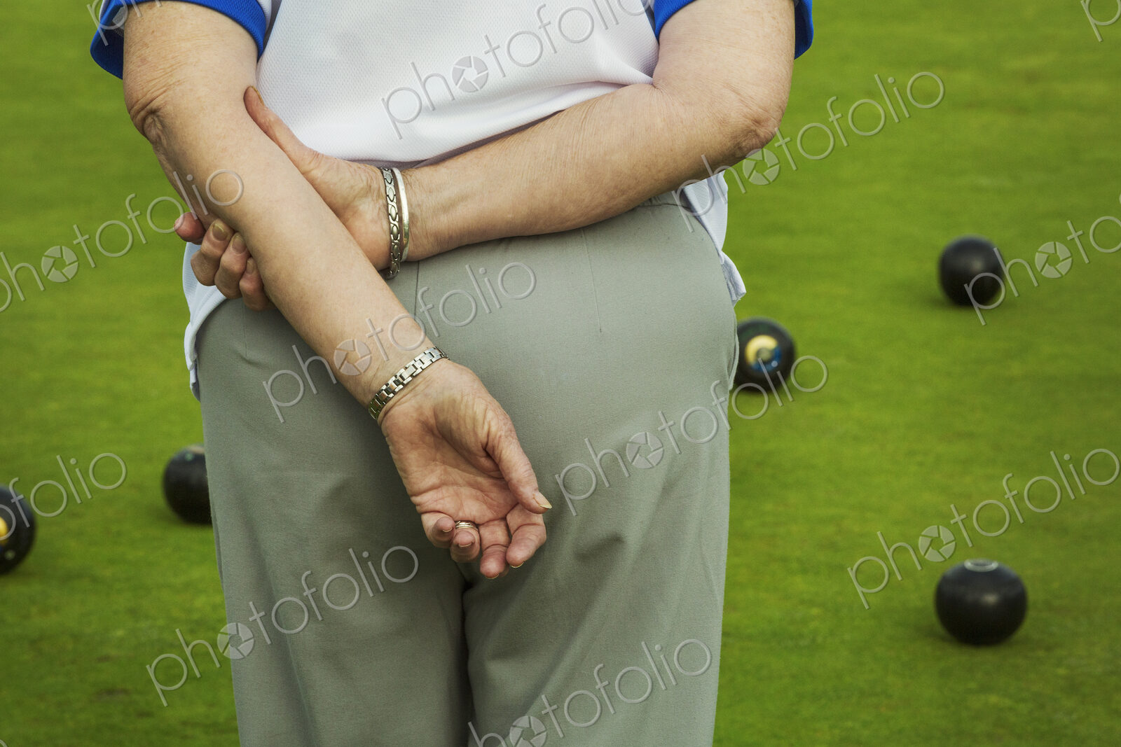 Rear view of a woman lawn bowls player with hands behind her back, and lawn bowls…