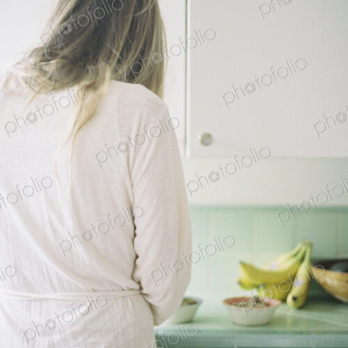 Rear view of a woman standing in a kitchen, preparing breakfast.