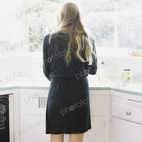 Rear view of a woman with long blond hair standing at a kitchen sink.