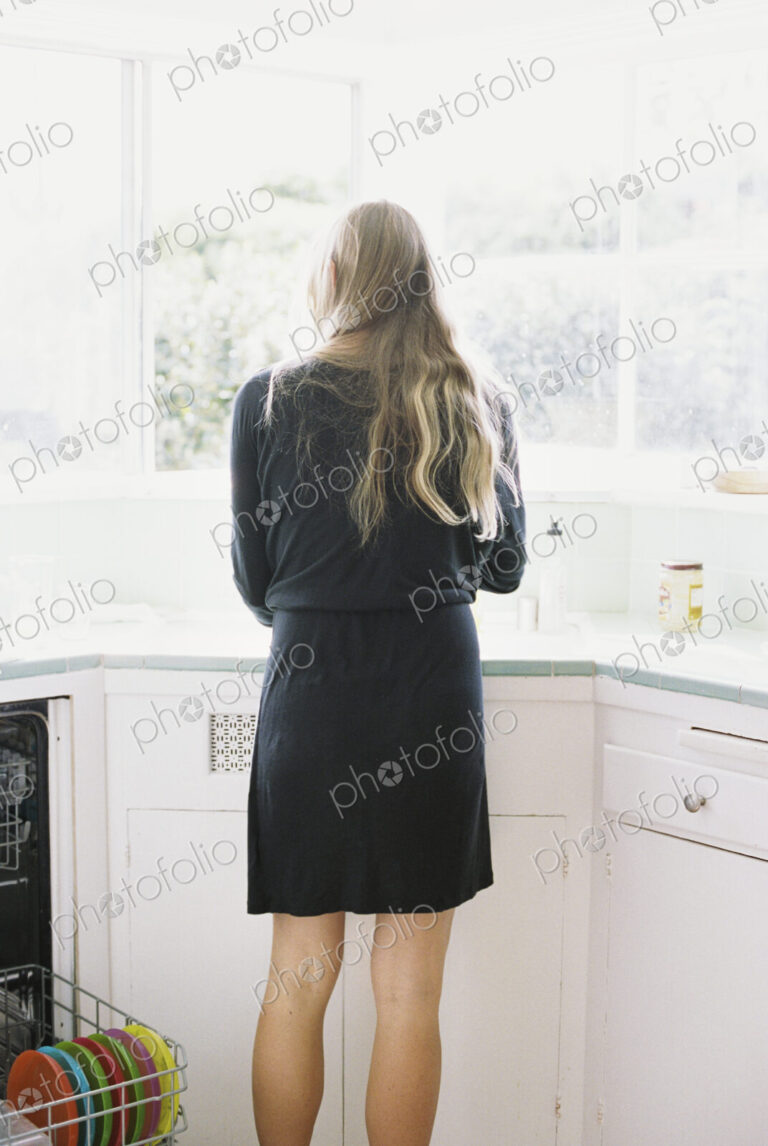 Rear view of a woman with long blond hair standing at a kitchen sink.