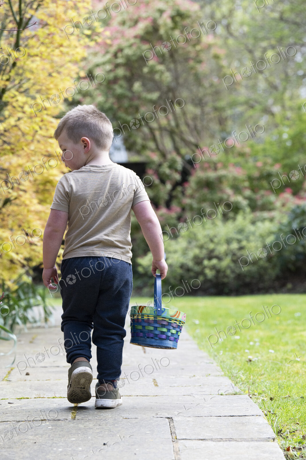 Rear view of boy walking along a garden path, carrying a basket with Easter Eggs.