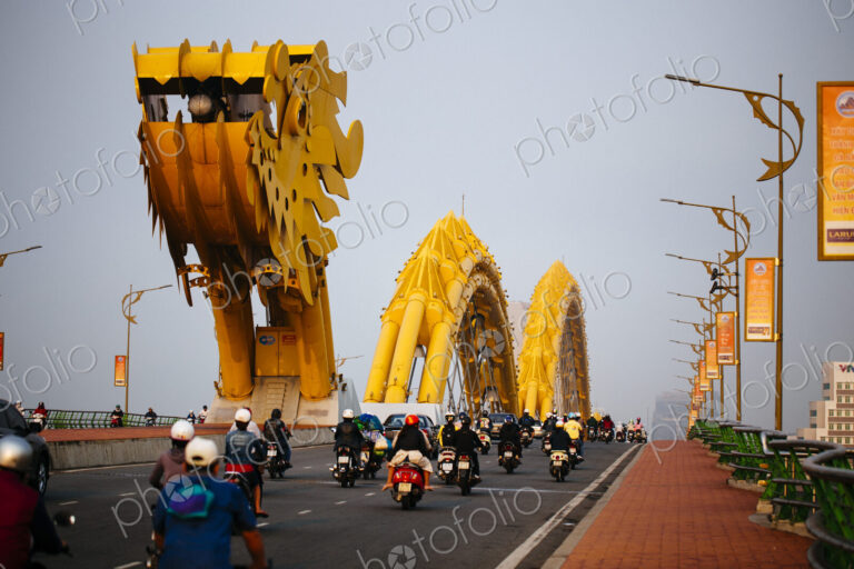 Rear view of commuters on motorcycles crossing bridge in the shape of a dragon.