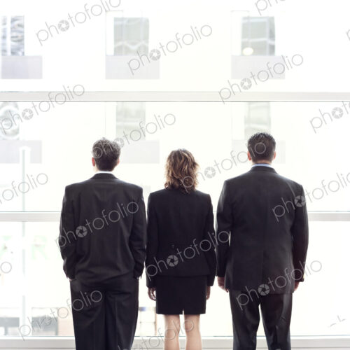 Rear view of group of three business people looking out the window of a conference…
