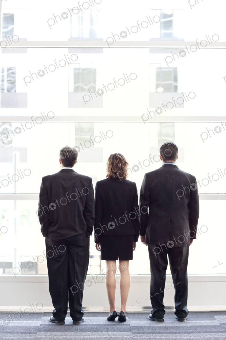 Rear view of group of three business people looking out the window of a conference…
