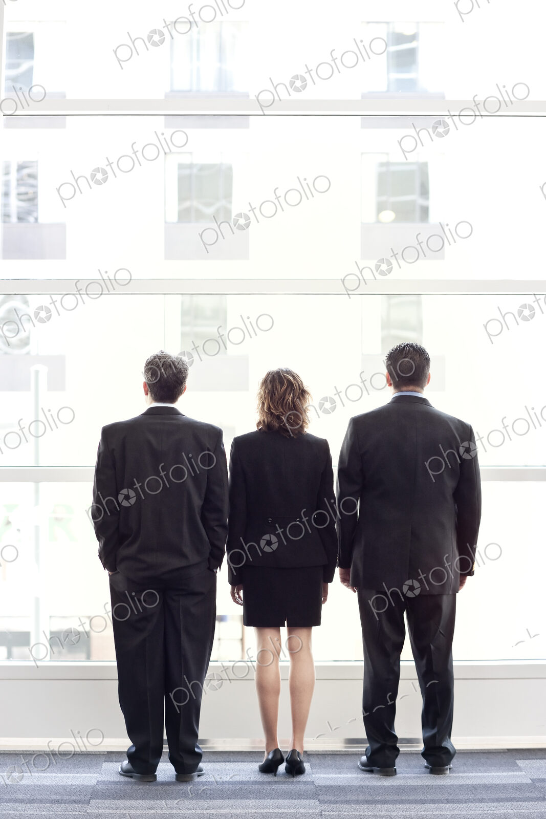 Rear view of group of three business people looking out the window of a conference…