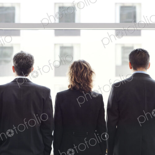 Rear view of group of three business people looking out the window of a conference…