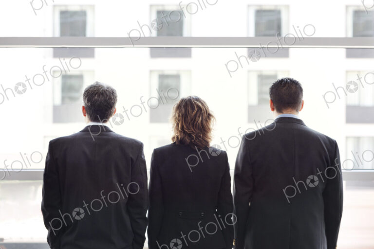 Rear view of group of three business people looking out the window of a conference…
