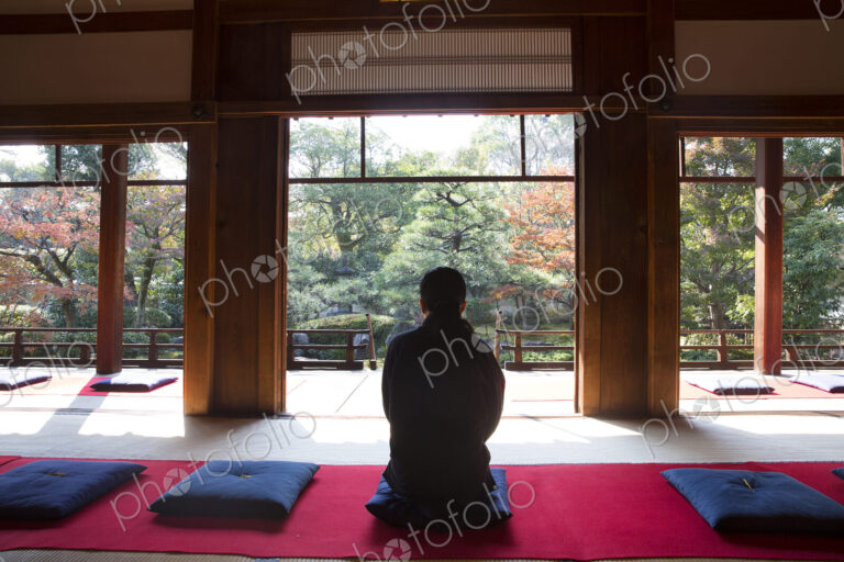 Rear view of man sitting on blue cushion on floor in traditional Japanese building.