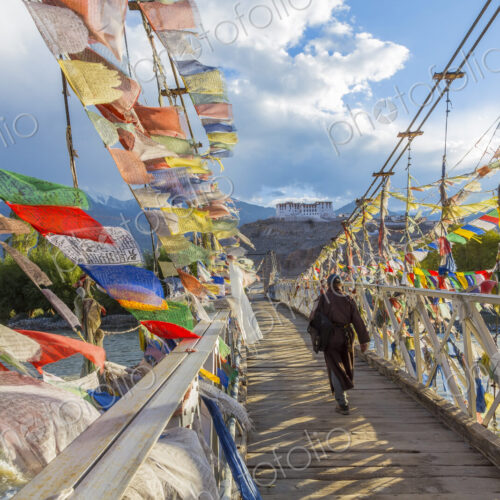 Rear view of man walking across bridge decorated with colourful prayer flags.