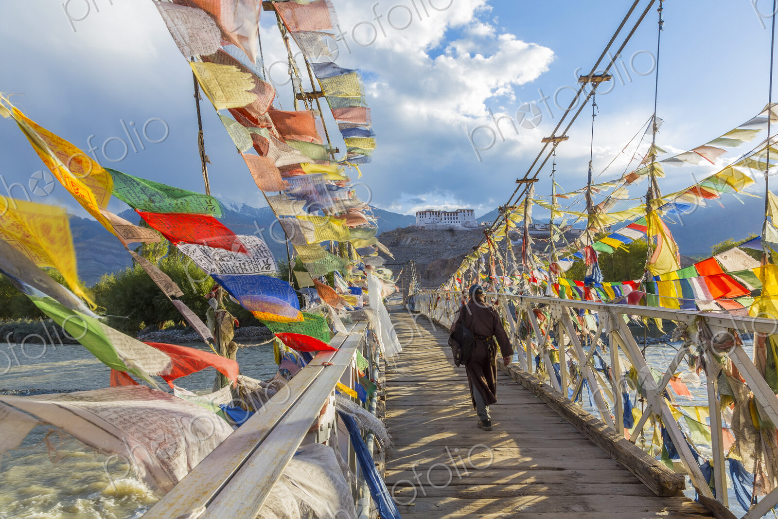 Rear view of man walking across bridge decorated with colourful prayer flags.