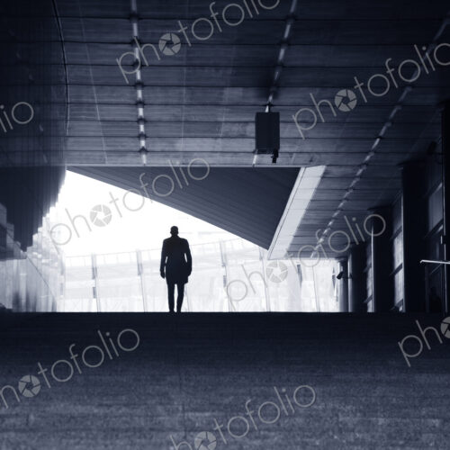 Rear view of man wearing coat and bowler hat standing at top of stairway of concrete…