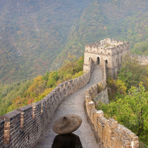 Rear view of man wearing traditional straw hat standing on Great Wall of China.