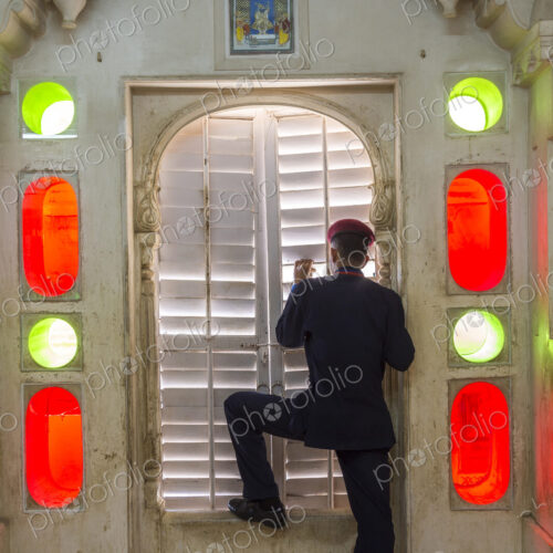Rear view of man wearing uniform standing at a closed door, looking through shutters.