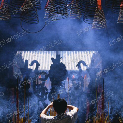 Rear view of person standing in front of shrine with incense burners.