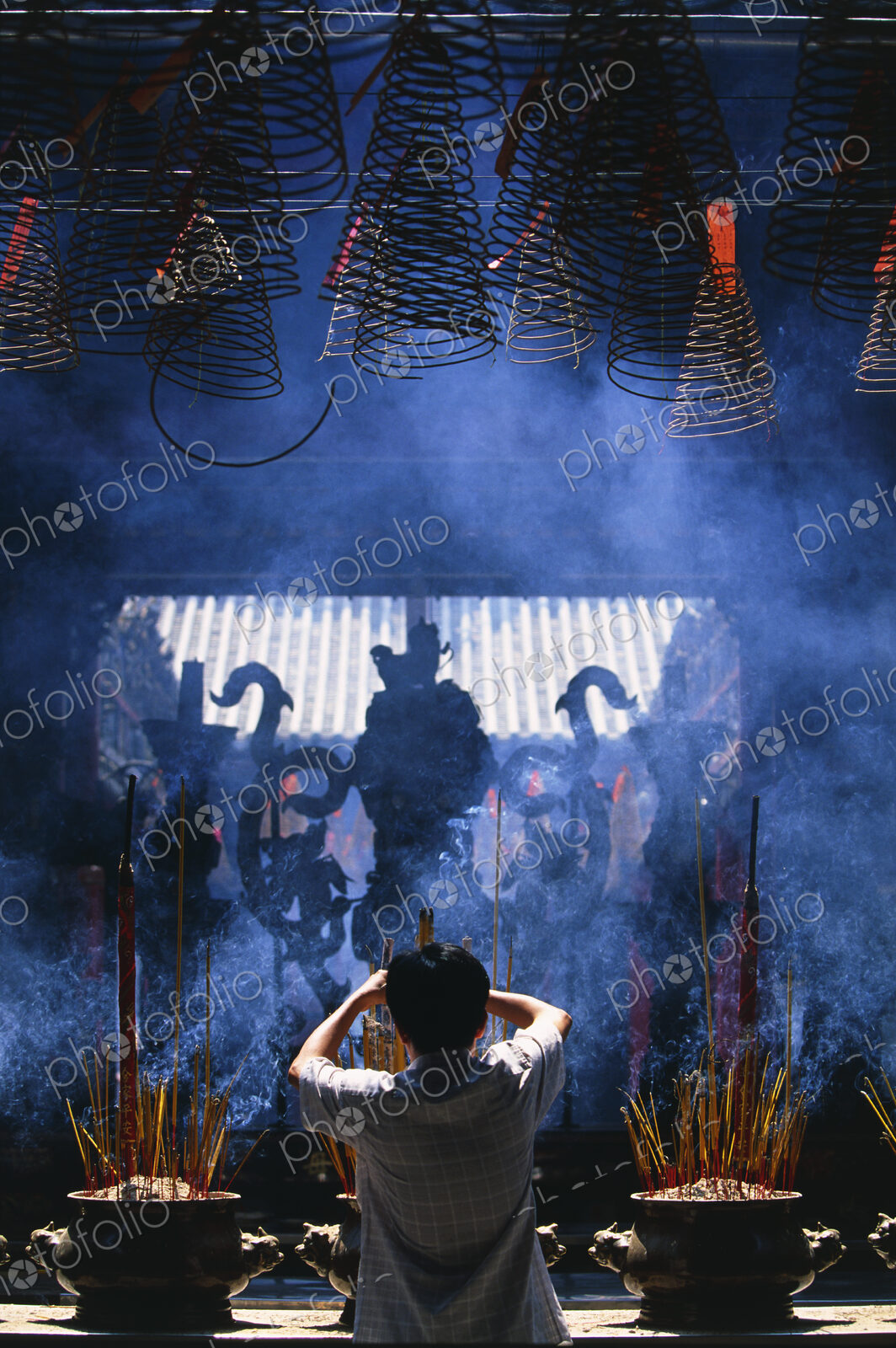 Rear view of person standing in front of shrine with incense burners.