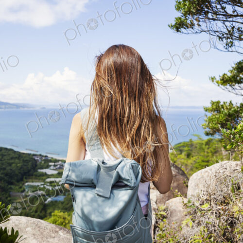 Rear view of woman carrying backpack standing on a rock on cliff, ocean in the background. Rear view of woman carrying backpack standing on a rock on cliff, ocean in the background.
