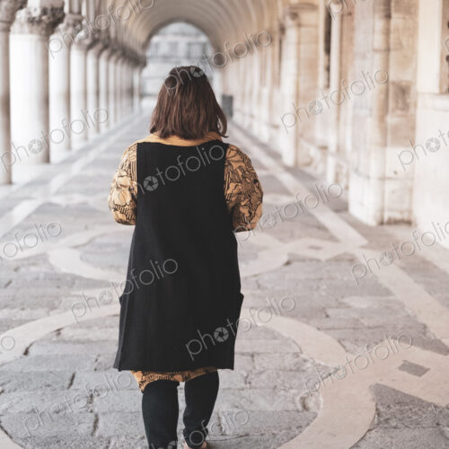 Rear view of woman walking along a colonnade in Venice, Veneto, Italy.