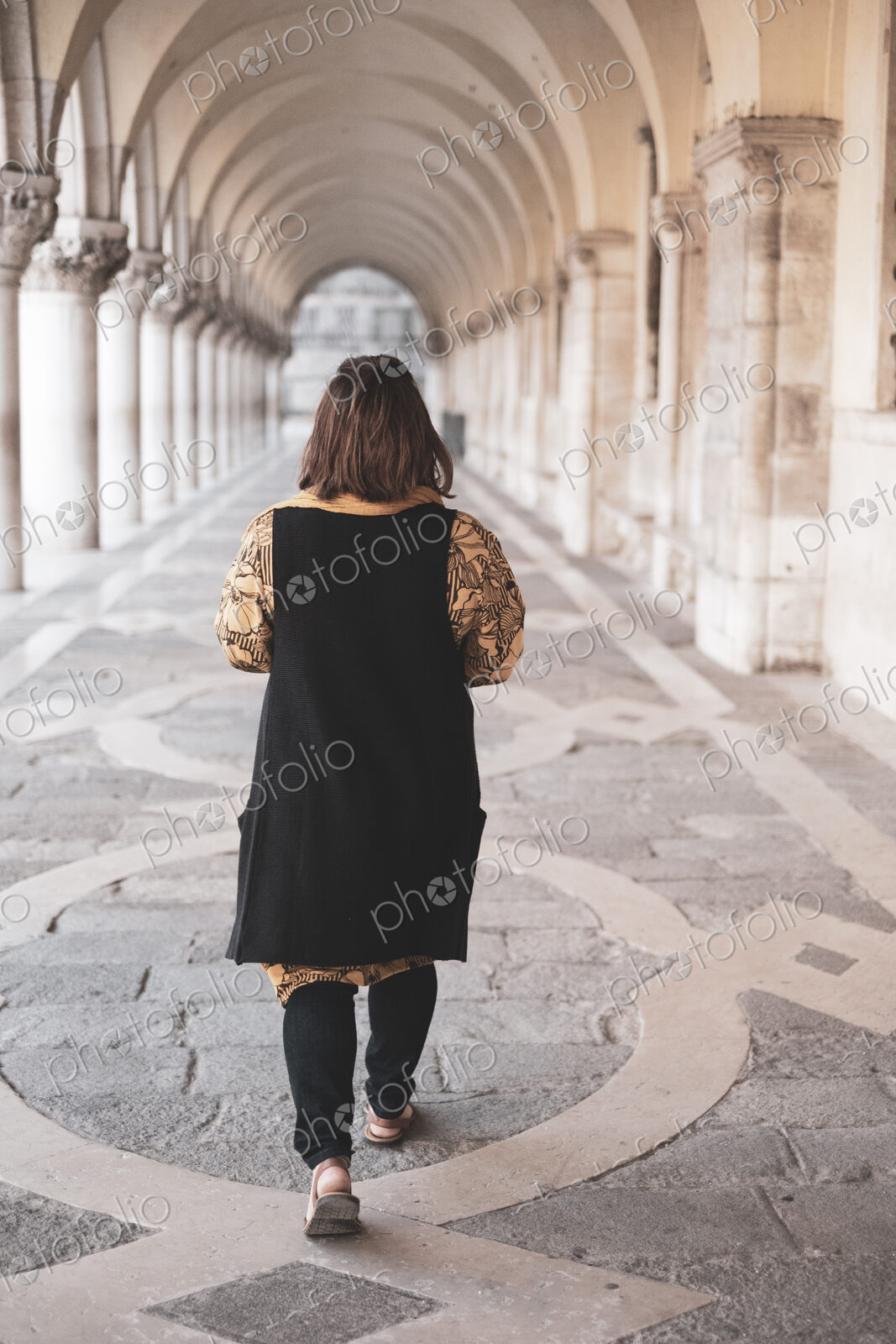 Rear view of woman walking along a colonnade in Venice, Veneto, Italy.