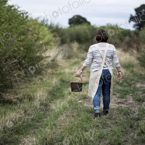 Rear view of woman walking along rural path, carrying brown wicker basket. Rear view of woman walking along rural path, carrying brown wicker basket.