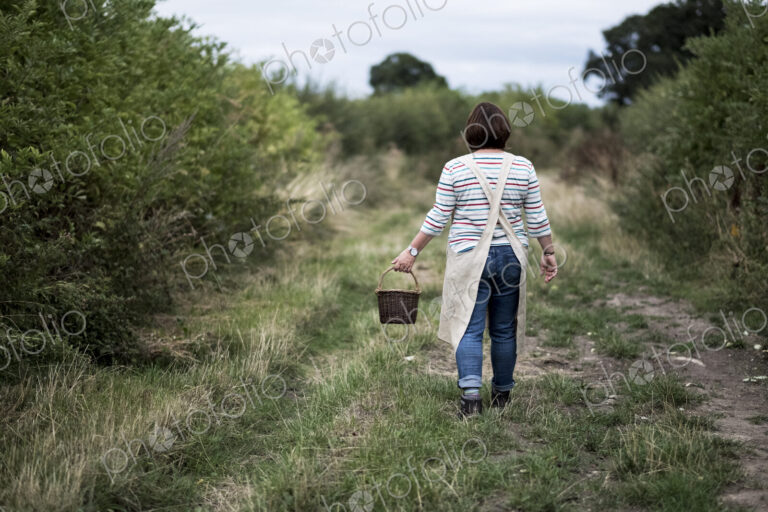 Rear view of woman walking along rural path, carrying brown wicker basket.