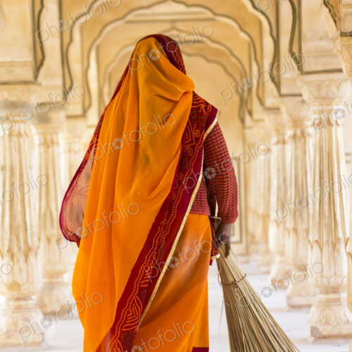 Rear view of woman wearing orange sari using broom to sweep floor of a colonnade. Rear view of woman wearing orange sari using broom to sweep floor of a colonnade.
