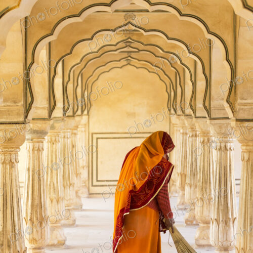 Rear view of woman wearing orange sari using broom to sweep floor of a colonnade. Rear view of woman wearing orange sari using broom to sweep floor of a colonnade.