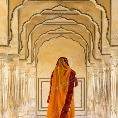Rear view of woman wearing orange sari walking along a colonnade.
