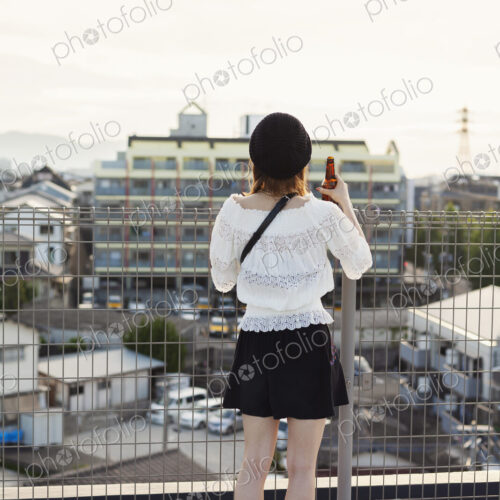Rear view of young Japanese woman standing on a rooftop in an urban setting.