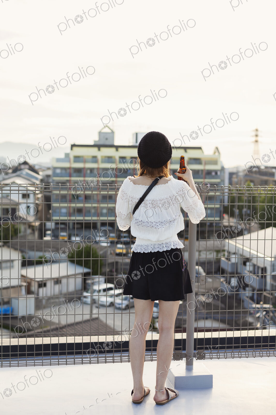 Rear view of young Japanese woman standing on a rooftop in an urban setting.