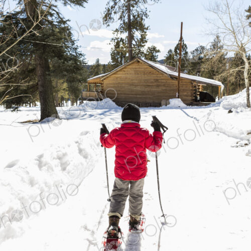 Rear view of young boy in a red jacket snow shoeing