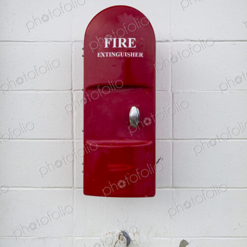 Red Fire Extinguisher mounted onto a white painted wall in a building. Red Fire Extinguisher mounted onto a white painted wall in a building.