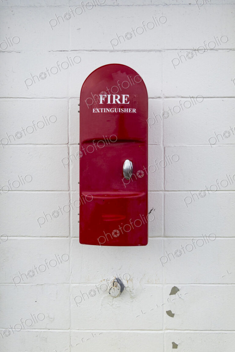 Red Fire Extinguisher mounted onto a white painted wall in a building.