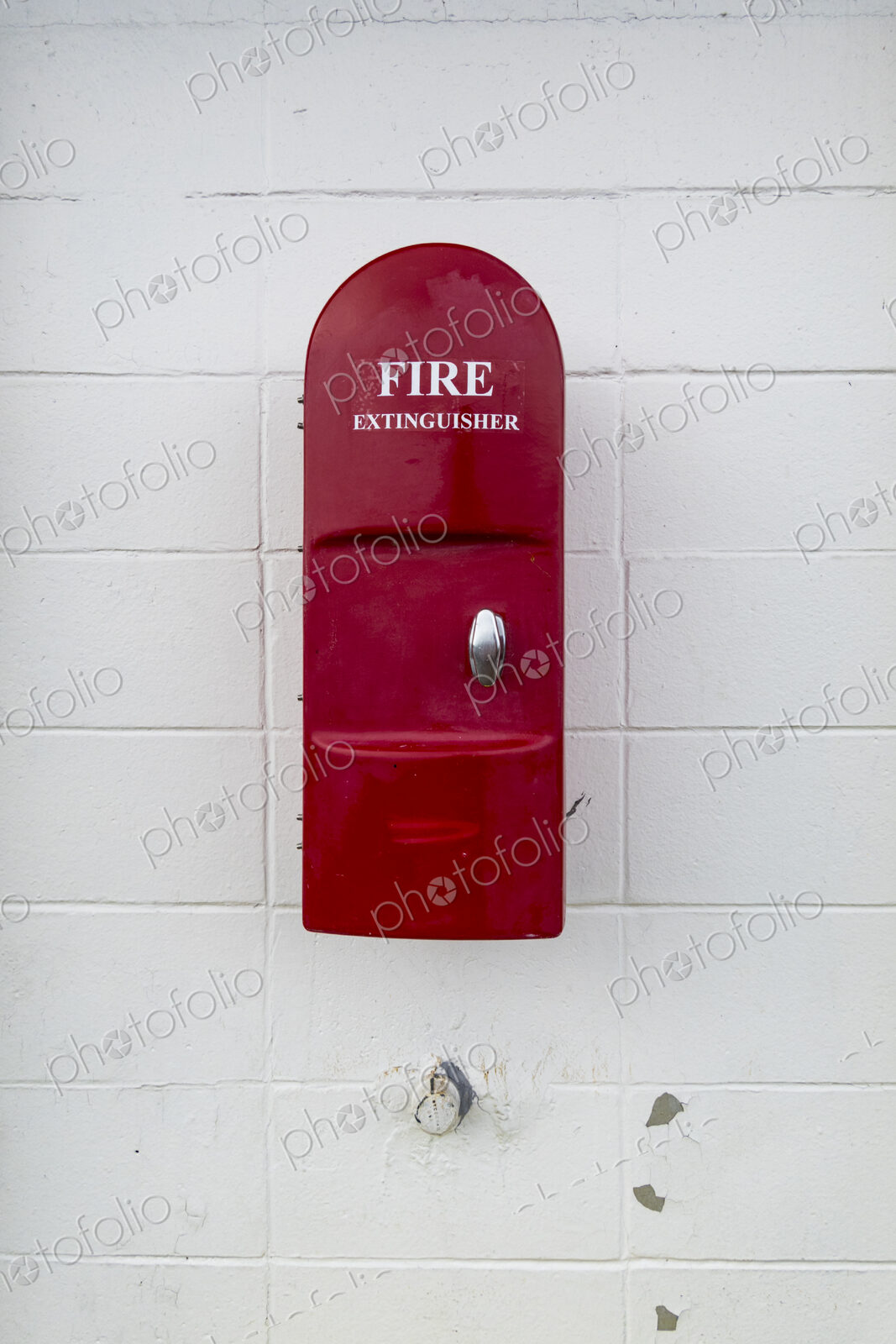Red Fire Extinguisher mounted onto a white painted wall in a building.