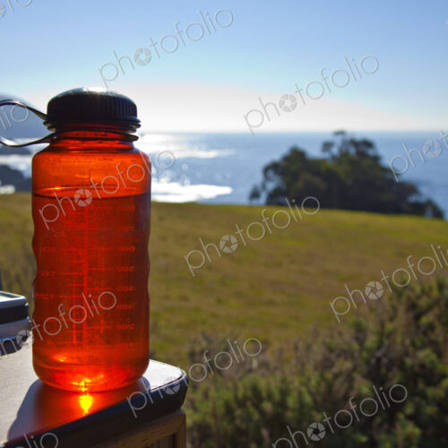 Red Water Bottle with Ocean in Background Red Water Bottle with Ocean in Background