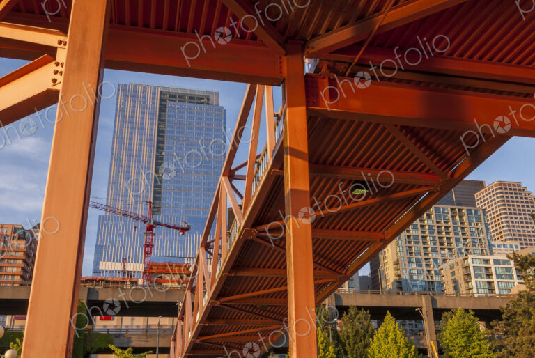 Red bridge seen from below with high rise buildings and contruction sites in background.