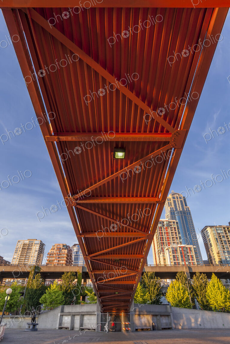 Red bridge seen from below with high rise buildings and contruction sites in background.