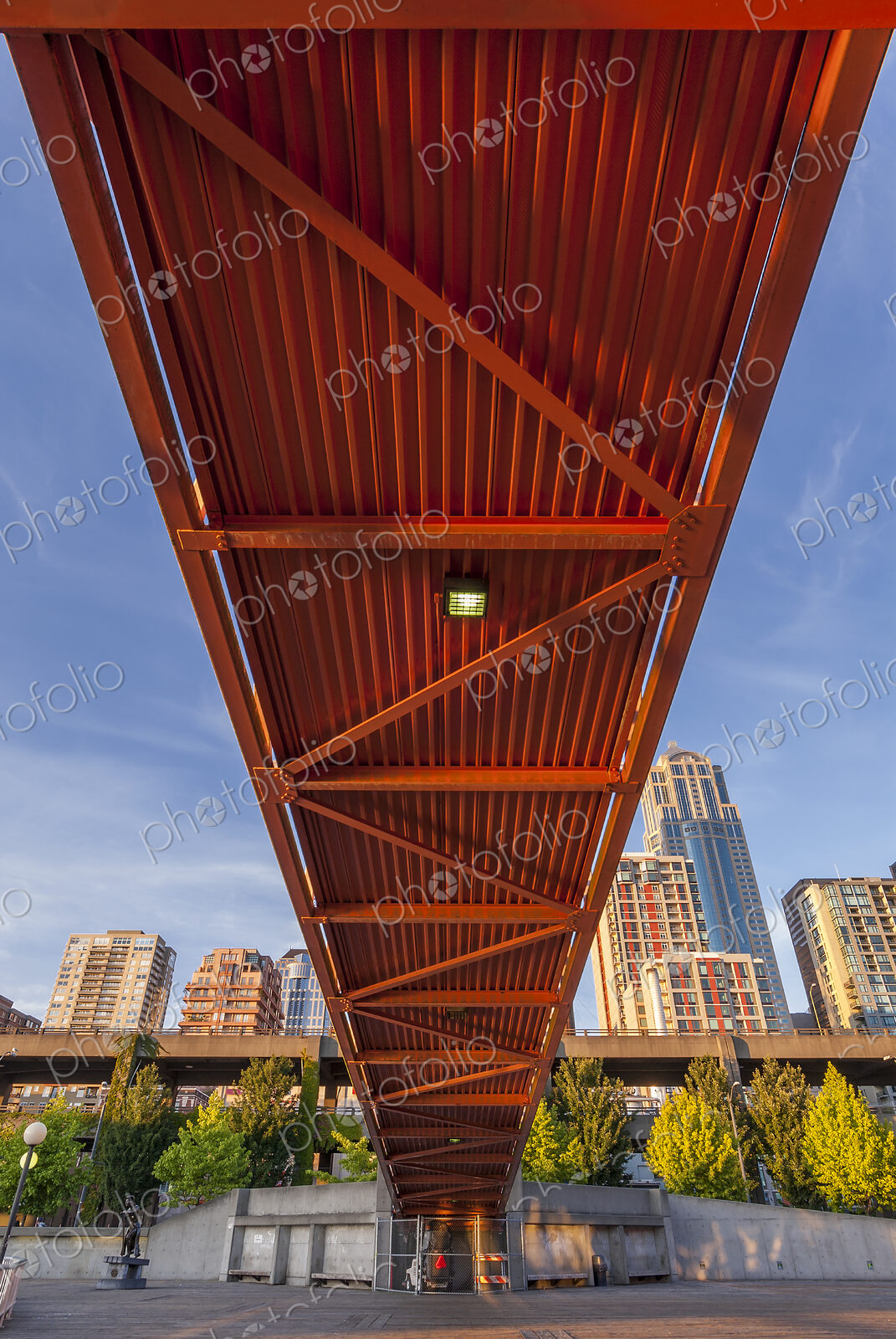 Red bridge seen from below with high rise buildings and contruction sites in background.