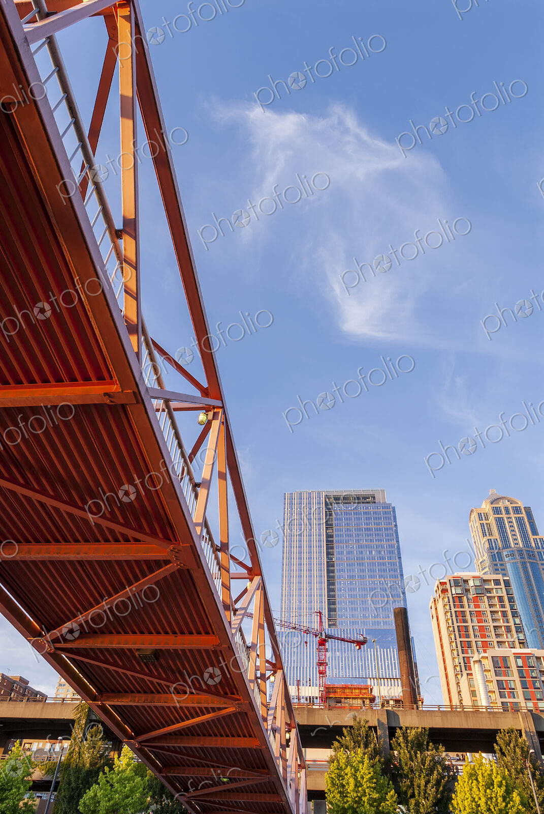 Red bridge seen from below with high rise contruction sites in background.