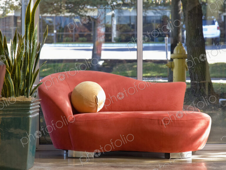 Red chaise longue and potted plant in office or hotel lobby.
